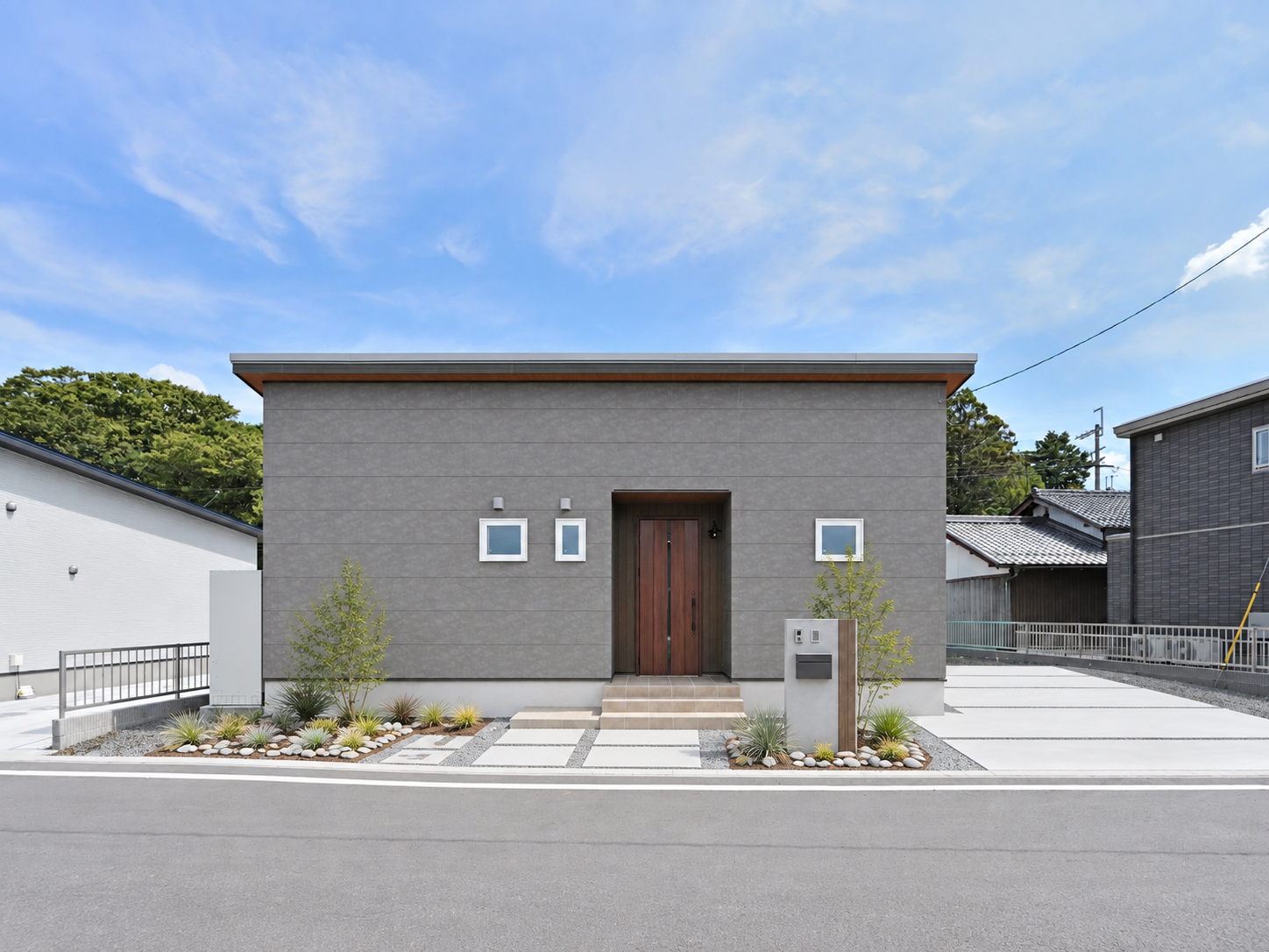 グレーの外壁と木目調の玄関ドアが特徴的な平屋の正面外観。玄関までのアプローチが見える住まい