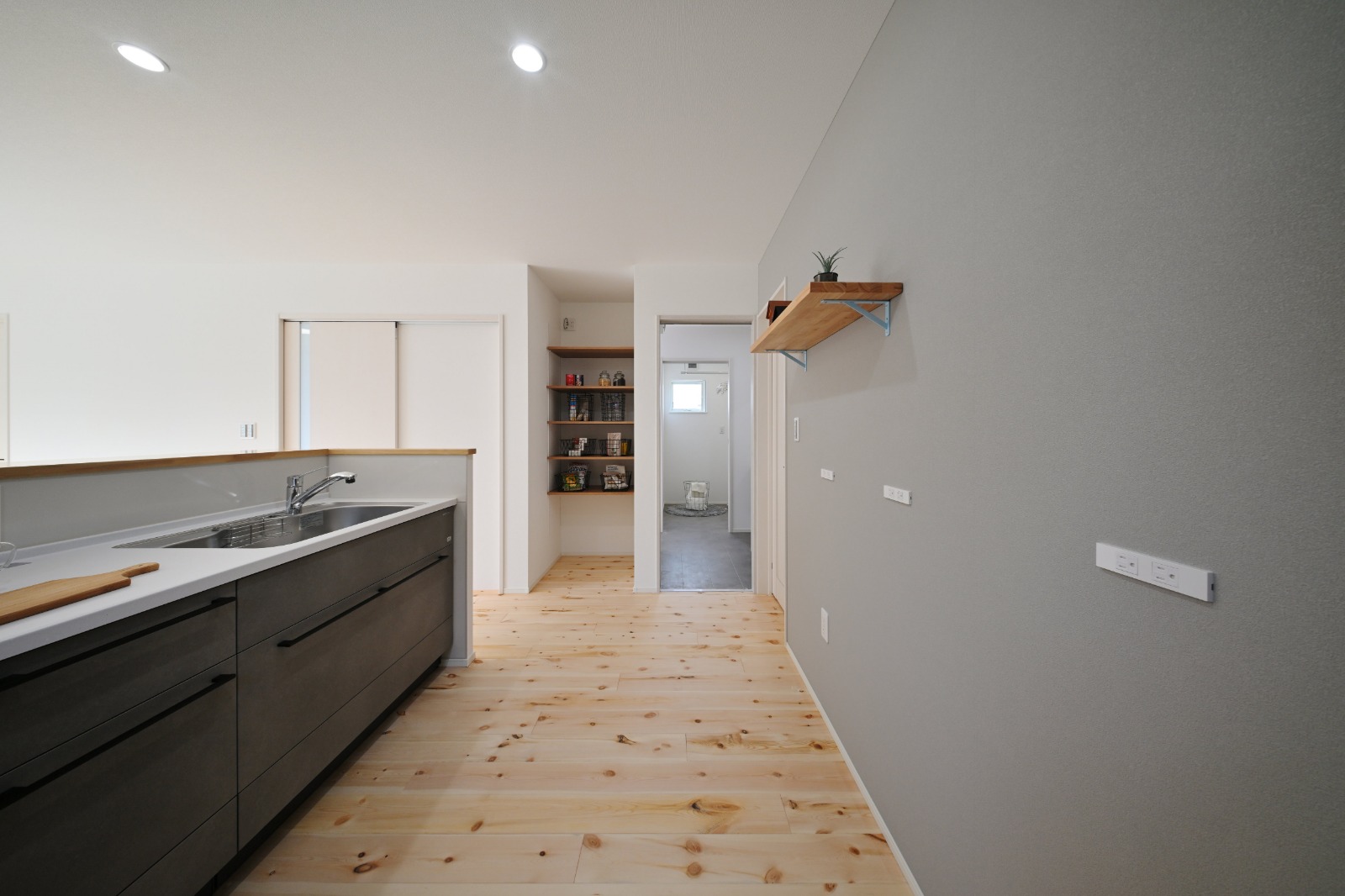 グレーのアクセントクロスが印象的な平屋のキッチン。壁面のスイッチやコンセント、奥の収納スペースが見える室内
